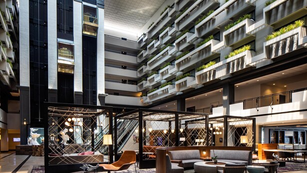 A modern hotel lobby with a central seating area, multiple floors with balconies, and a large staircase.