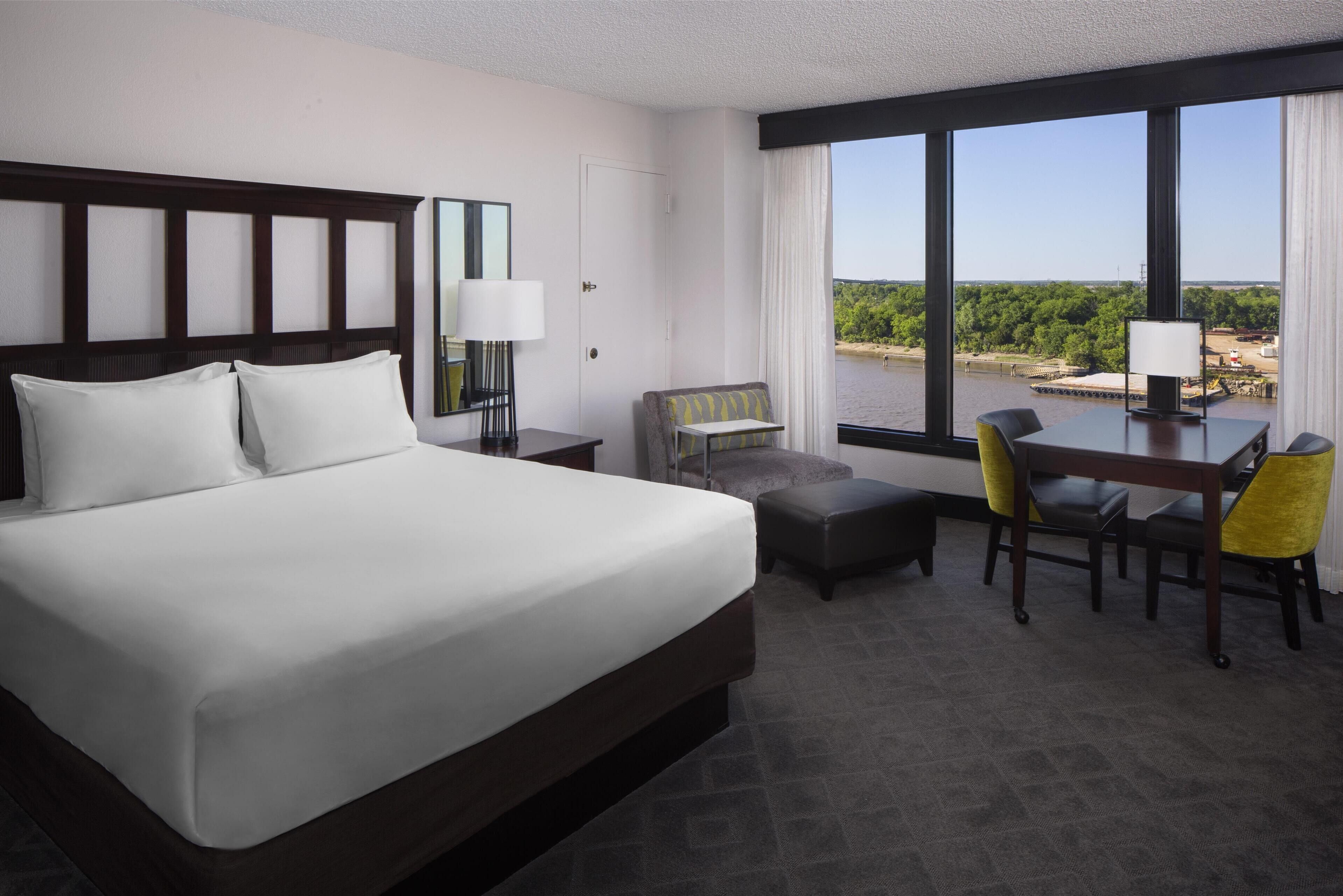 A hotel room with a large bed, a desk with two chairs, a small sofa, and a view of a body of water.