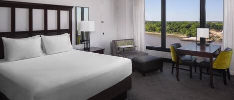 A hotel room with a large bed, a desk with two chairs, a small sofa, and a view of a body of water.