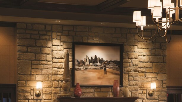 A cozy lounge area with a stone fireplace, comfortable seating, and a cityscape painting above the mantel. - DoubleTree by Hilton Cincinnati Airport (Florence)