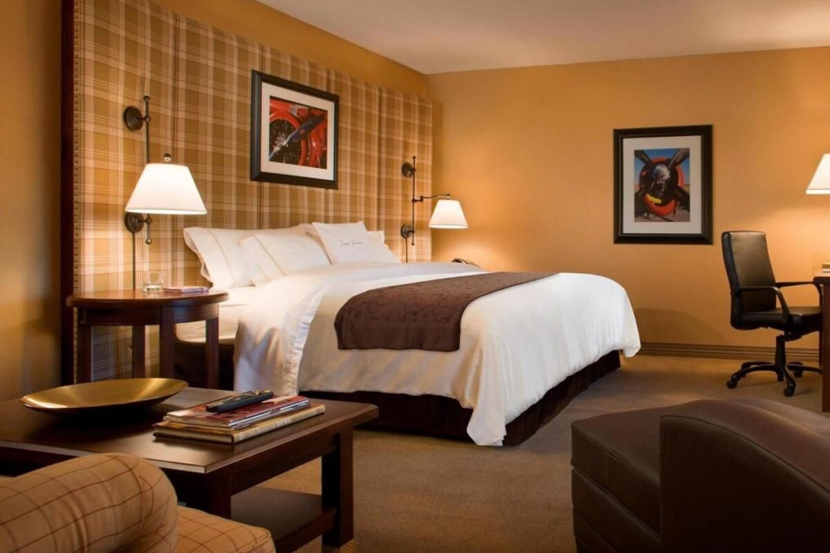 A hotel room with a bed, two bedside lamps, a desk with a chair, a couch, and two framed pictures on the wall.