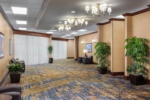 A hotel lobby with a patterned carpet, seating area, potted plants, and a chandelier. - DoubleTree by Hilton Cincinnati Airport (Florence)