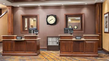 Un espace d’accueil d’hôtel comprenant deux comptoirs de réception en bois, une horloge murale et un miroir.