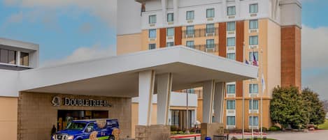 A hotel with a covered entrance, a van parked in front, and a flagpole with flags.