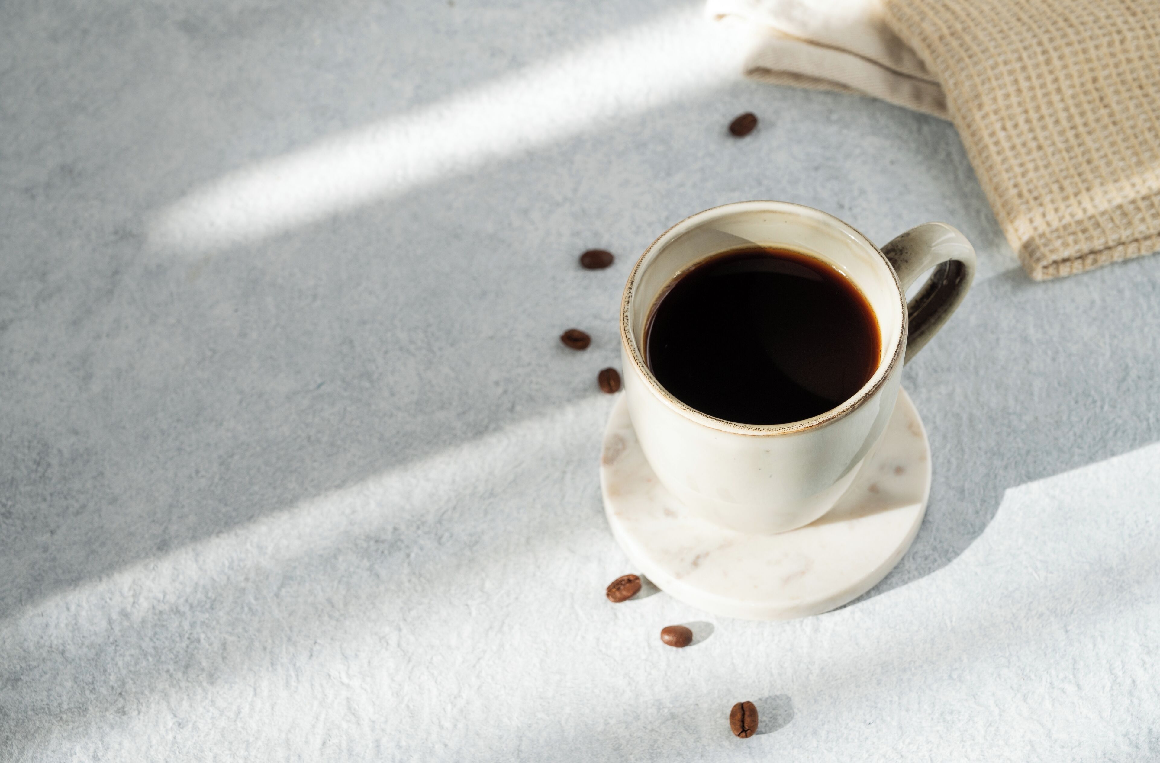 Una taza de café sobre una superficie de mármol con granos de café esparcidos.