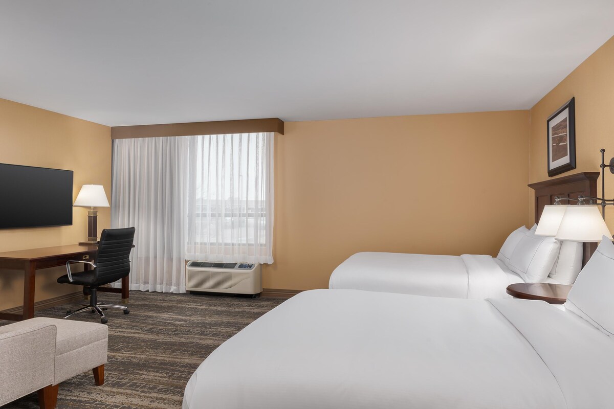 A hotel room with a bed, a desk, a chair, a television, and a window with curtains.