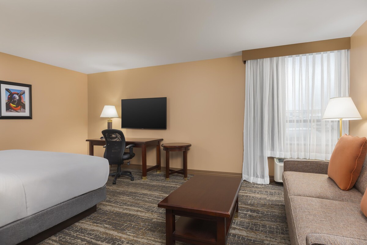 A hotel room with a bed, a desk, a chair, a television, a sofa, and a window with curtains.