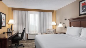A hotel room with a large bed, a desk with a chair, two bedside lamps, and a large window with curtains. - DoubleTree by Hilton Cincinnati Airport (Florence)