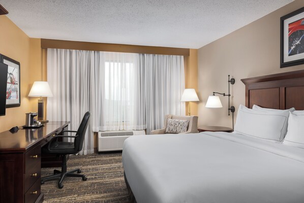 A hotel room with a large bed, a desk with a chair, two bedside lamps, and a large window with curtains. - DoubleTree by Hilton Cincinnati Airport (Florence)
