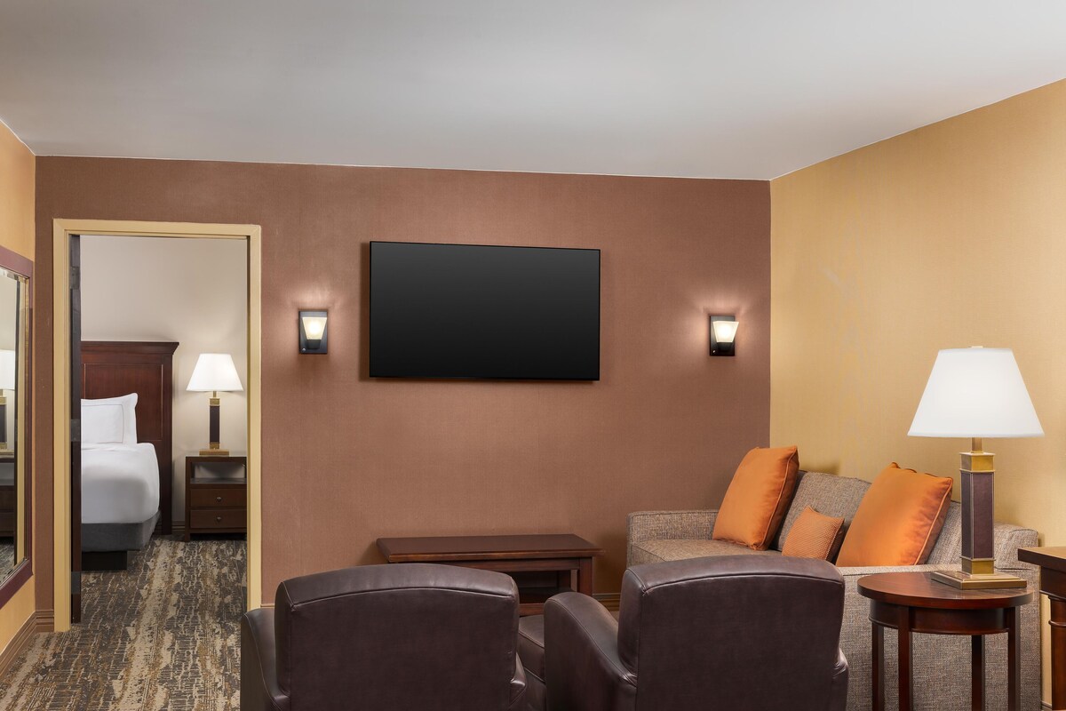 A hotel room with a bed, a desk, a sofa, two chairs, a flat-screen TV, and two wall-mounted lamps.