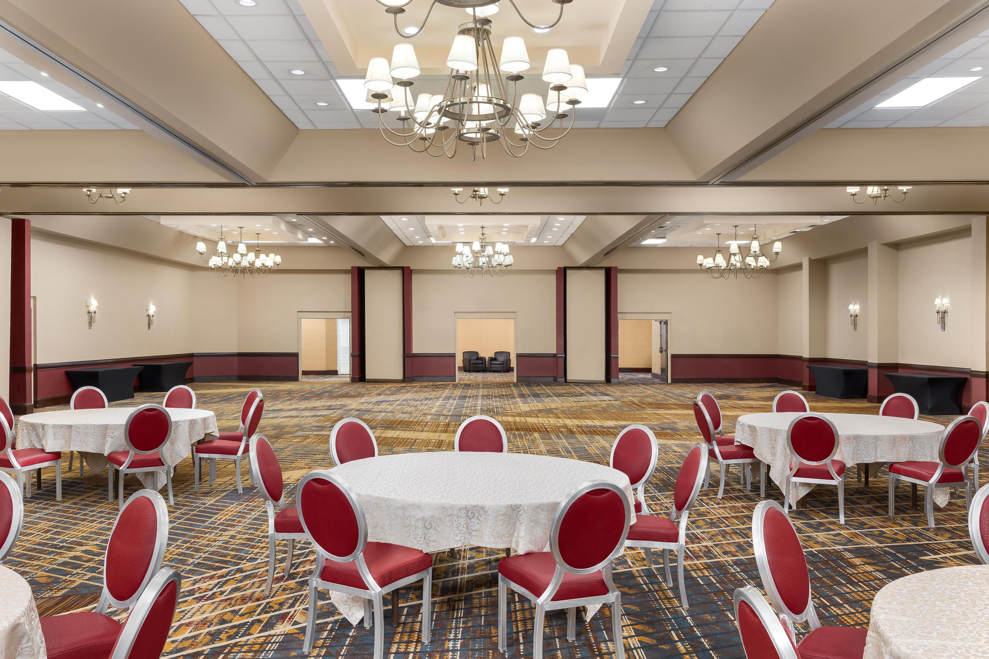 Une grande salle de conférence dotée de plusieurs tables rondes, de chaises rouges et de lustres.