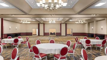 Une grande salle de conférence dotée de plusieurs tables rondes, de chaises rouges et de lustres.
