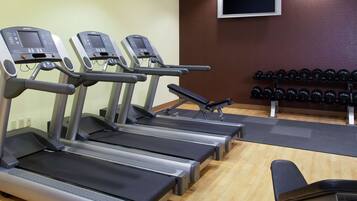 Un gimnasio con cintas de correr, una banca y un estante con mancuernas.