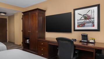 Una habitación de hotel con una cama, un escritorio con silla, un armario, un televisor de pantalla plana y un cuadro en la pared.