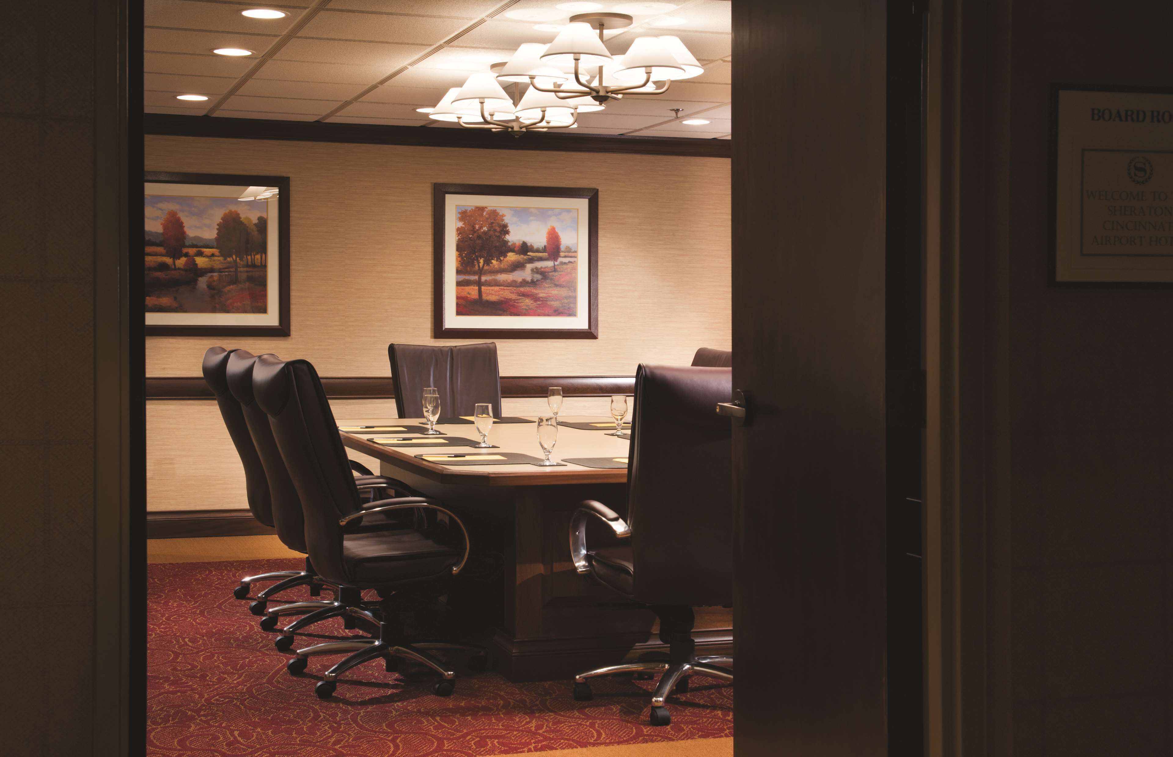 A conference room with a long table, multiple chairs, and framed landscape paintings on the wall.