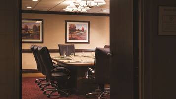A conference room with a long table, multiple chairs, and framed landscape paintings on the wall.