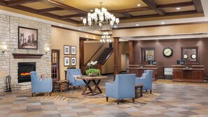 A lobby with a stone fireplace, blue armchairs, a chandelier, a staircase, and a reception desk with clocks. - DoubleTree by Hilton Cincinnati Airport (Florence)