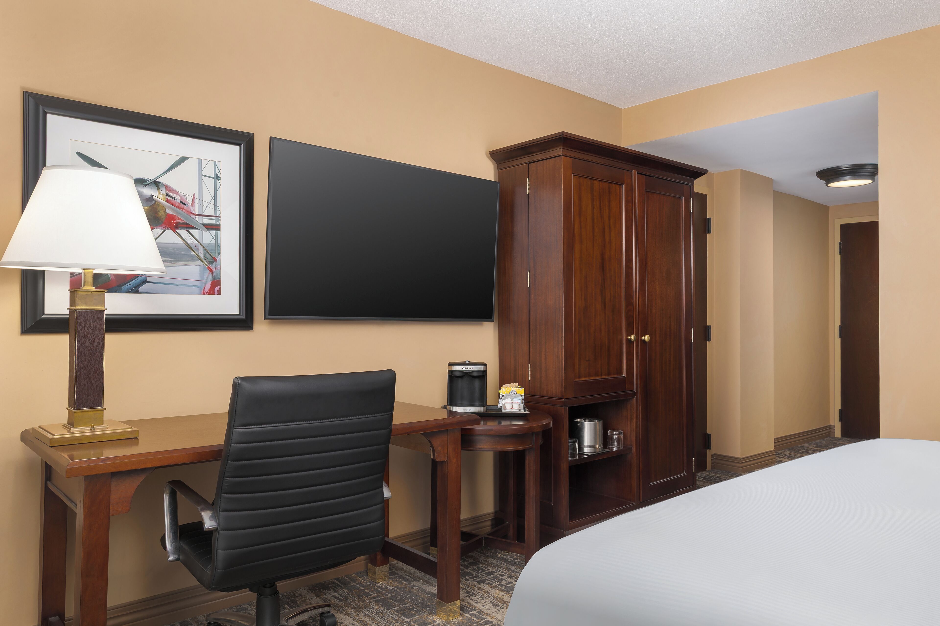 A hotel room with a bed, a desk with a chair, a cabinet, a framed picture on the wall, and a coffee maker on the desk.