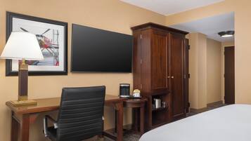 A hotel room with a bed, a desk with a chair, a cabinet, a framed picture on the wall, and a coffee maker on the desk.