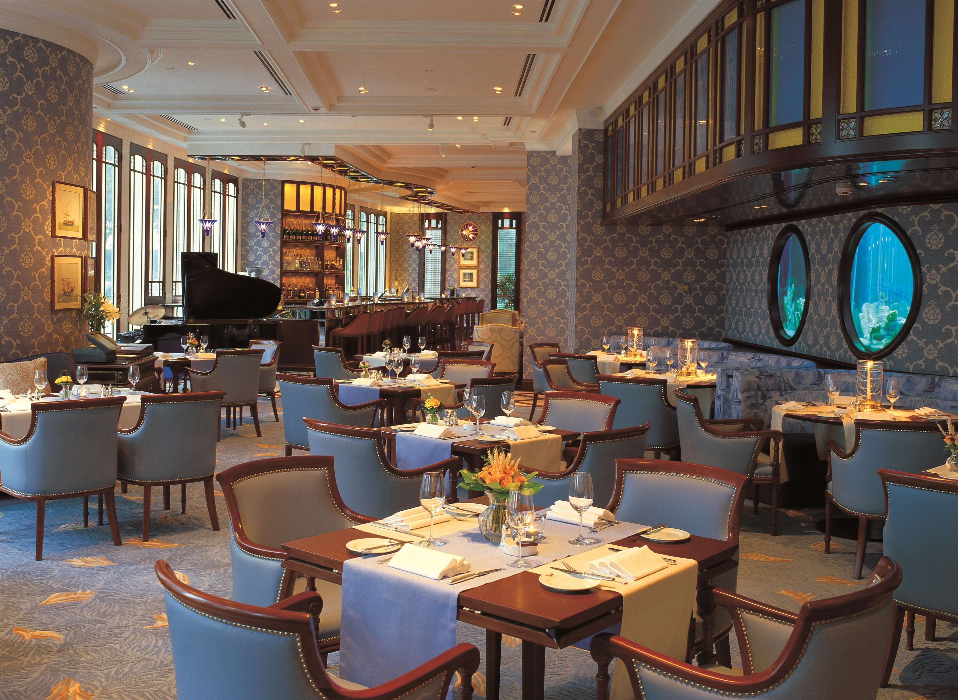 A spacious dining area with multiple tables and chairs, a piano, and large windows providing natural light.