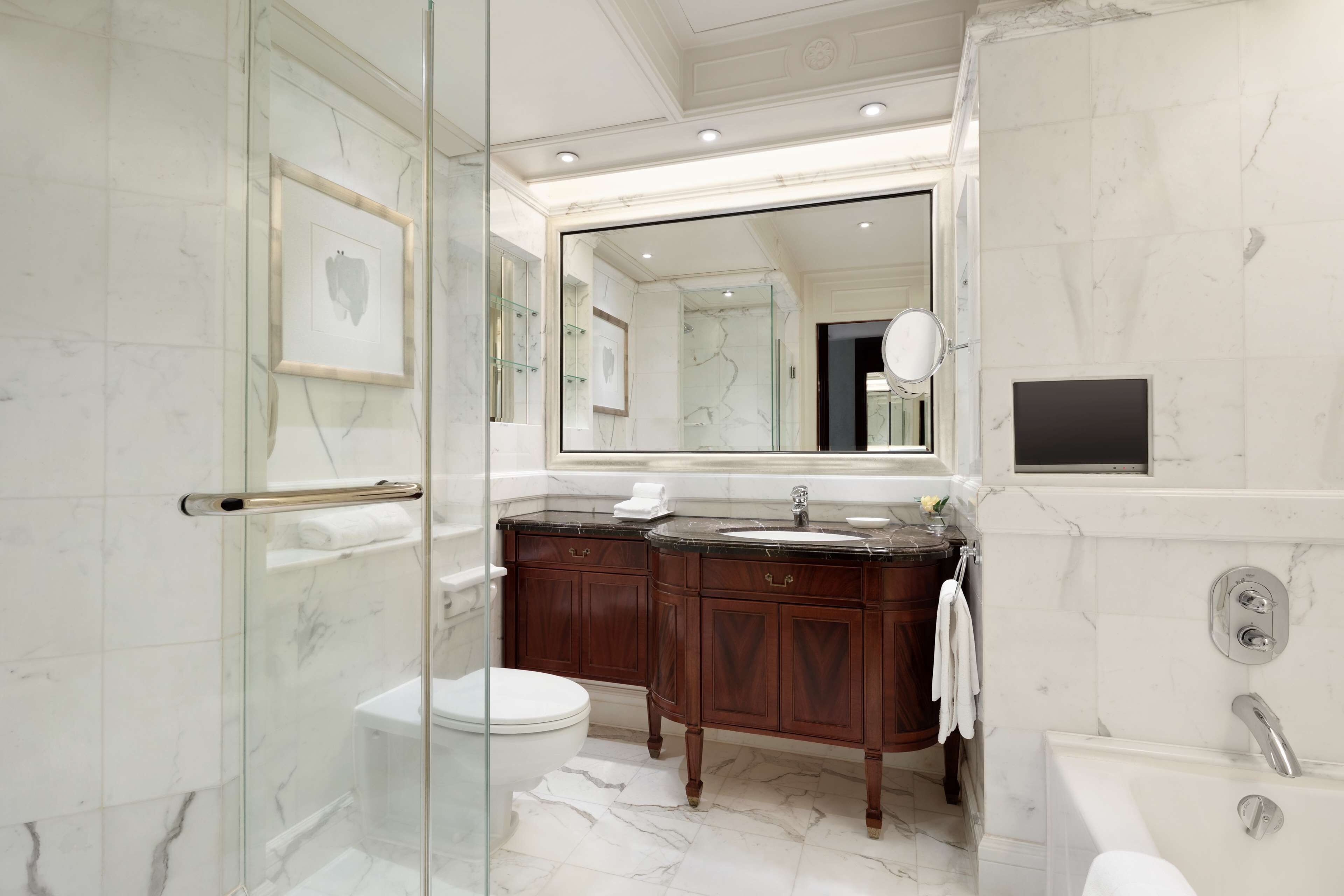 Un baño moderno con cabina de ducha de vidrio, un espejo grande, suelo de mármol y bañera empotrada.