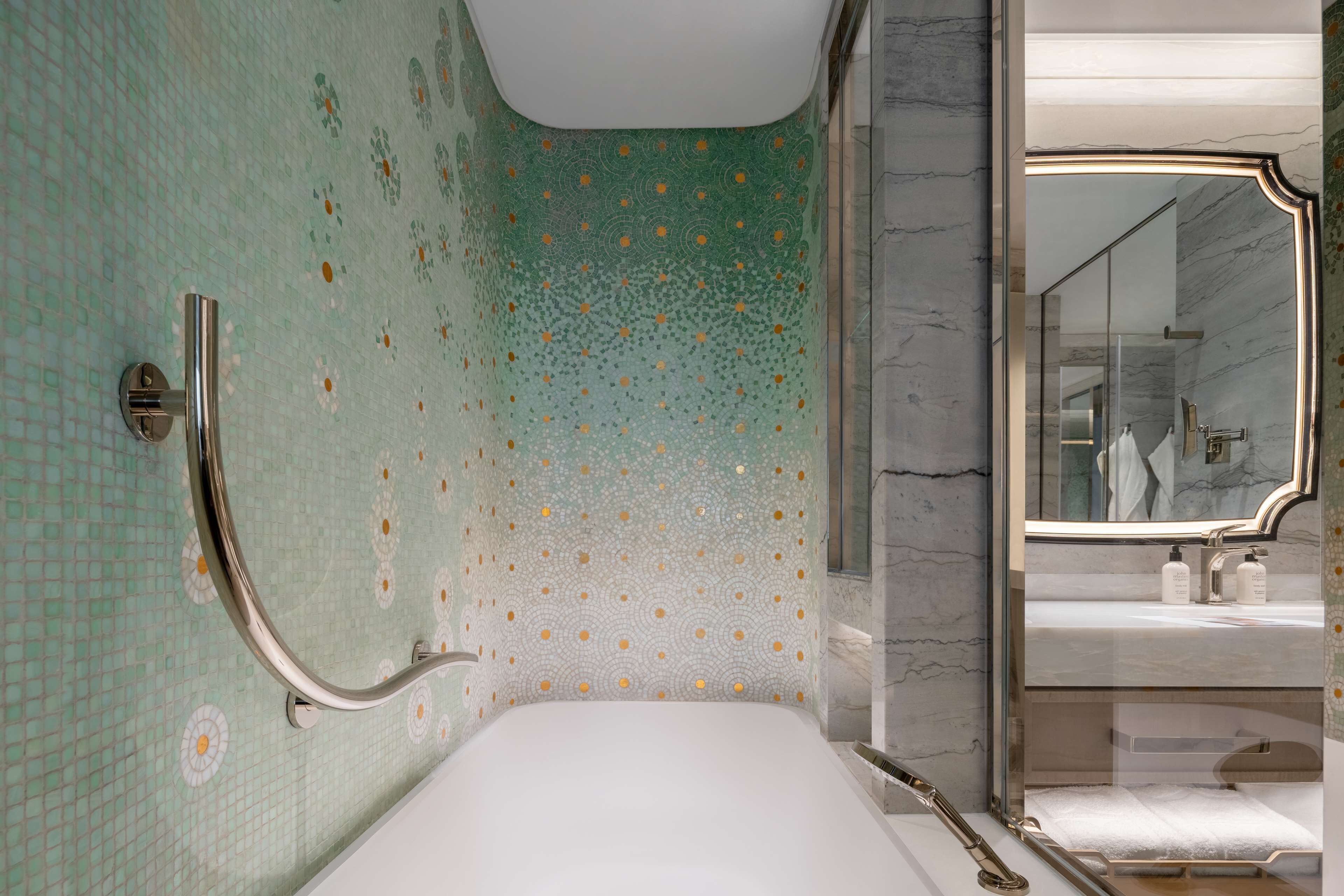 A bathroom with a patterned wall, a bathtub, a shower area, and a mirror reflecting a sink and towel.