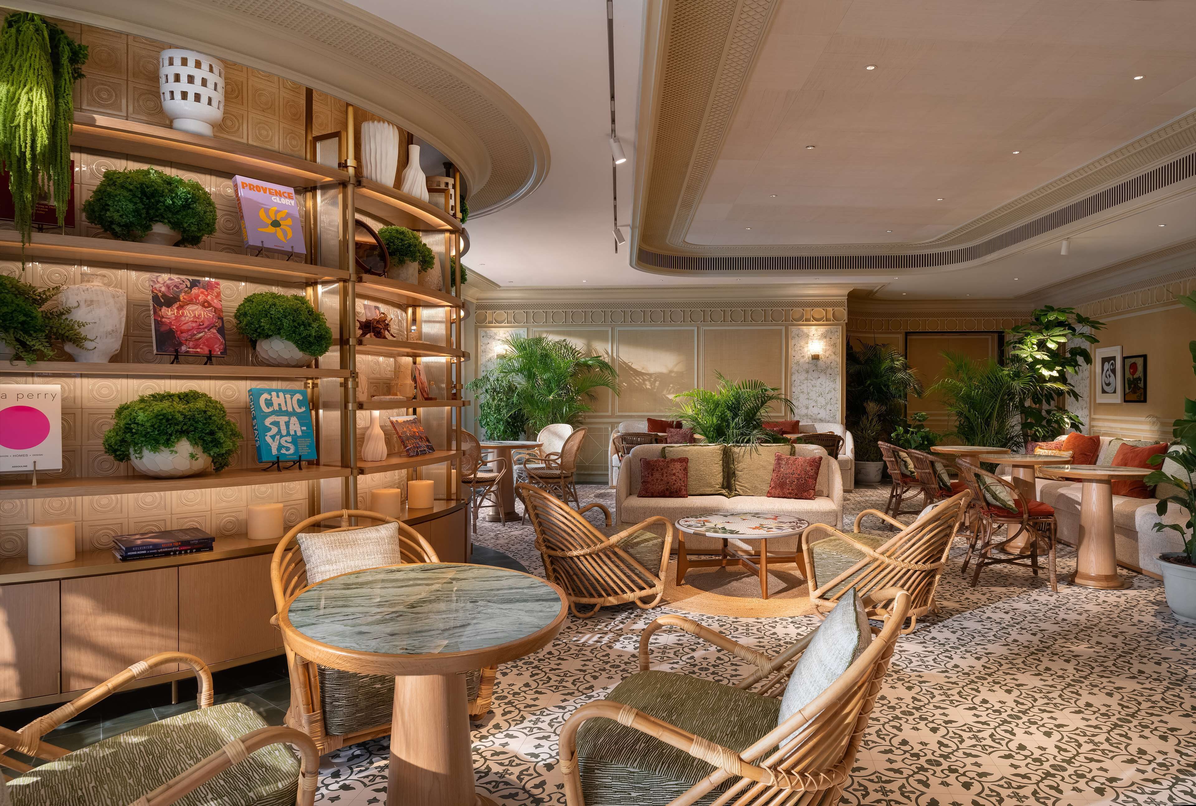 Een goed verlichte, elegant ingerichte lounge met rieten meubels, een marmeren tafel en diverse sierplanten.