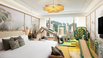 A hotel room with a bed, a desk, a chair, a sofa, a small slide, and a view of the city.