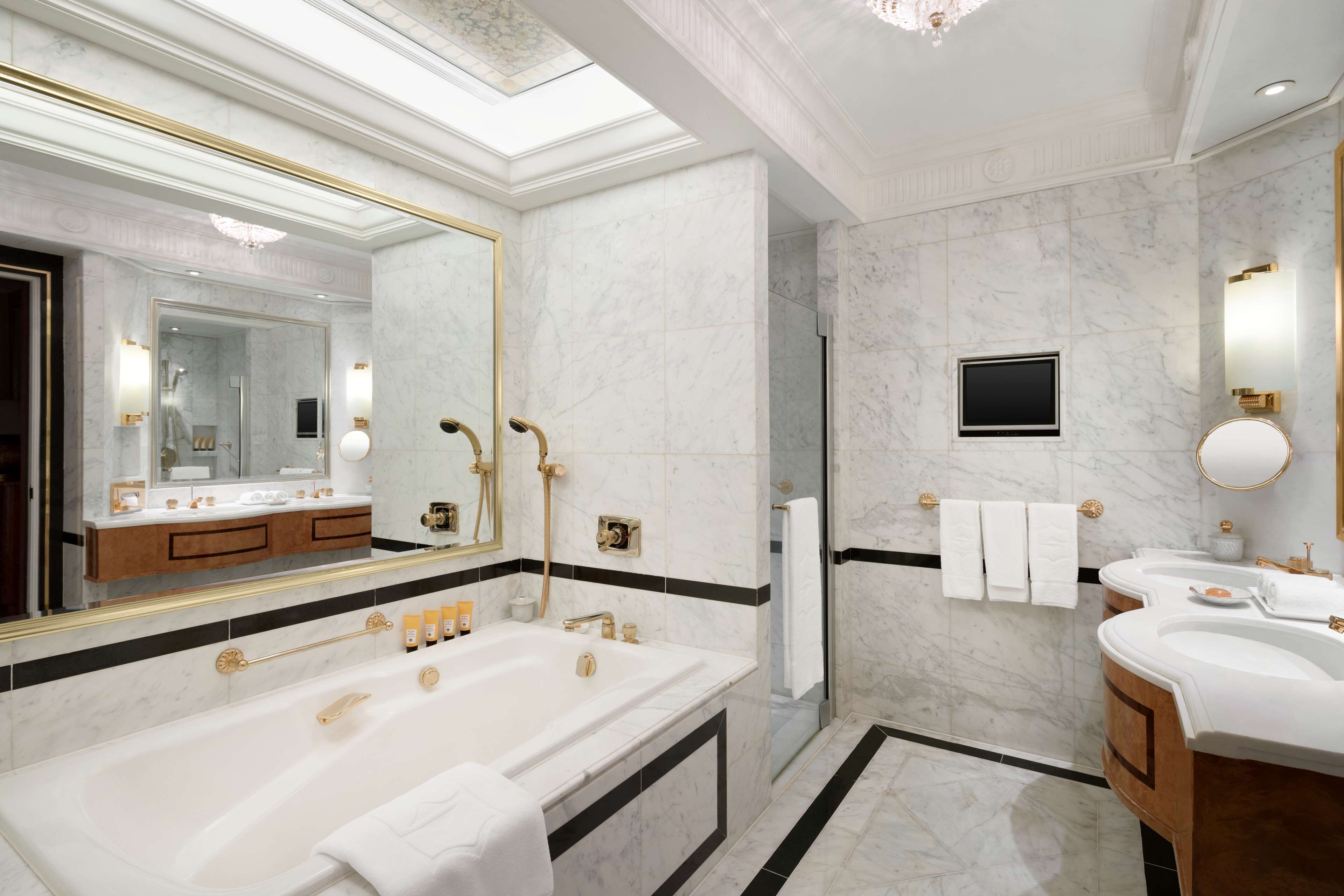 A luxurious bathroom with a large bathtub, two sinks, a shower, and a glass-enclosed shower area.