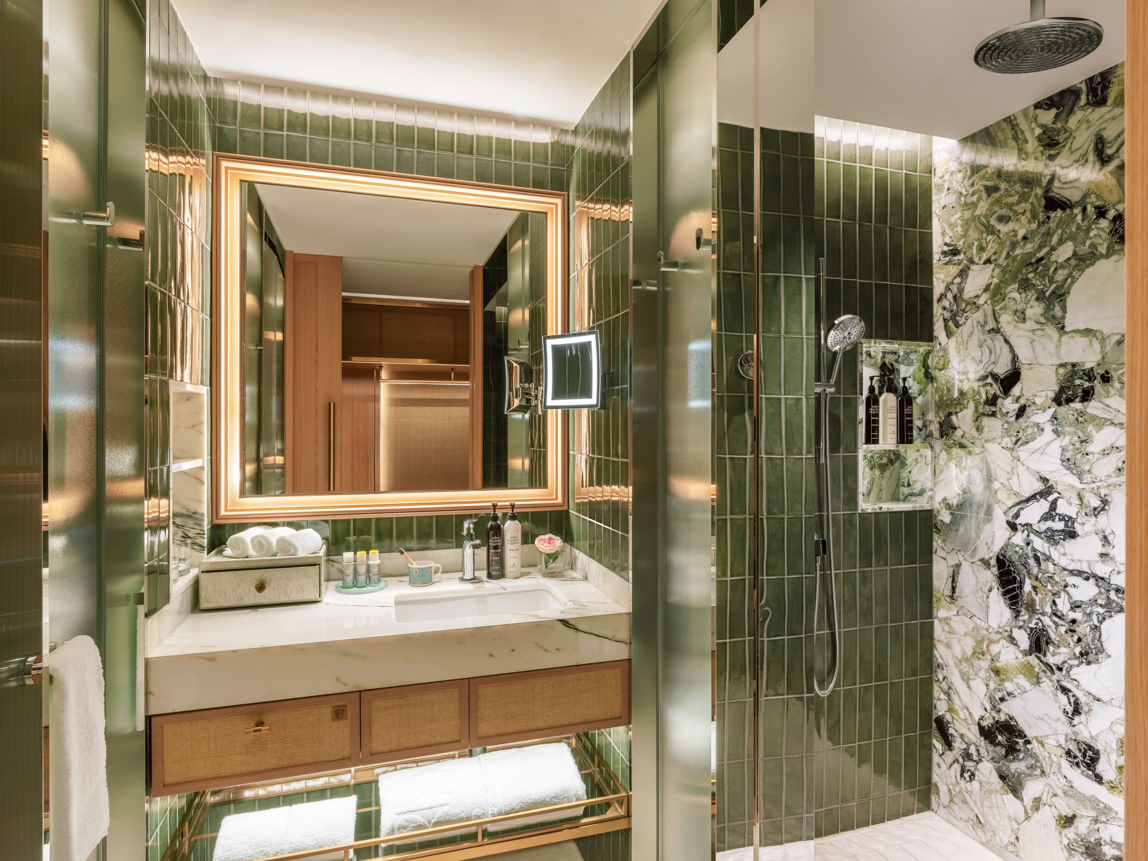 A modern bathroom with a large mirror, a shower with a glass door, and a vanity with toiletries.