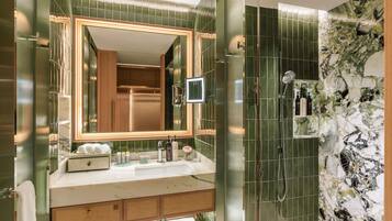 A modern bathroom with a large mirror, a shower with a glass door, and a vanity with toiletries.