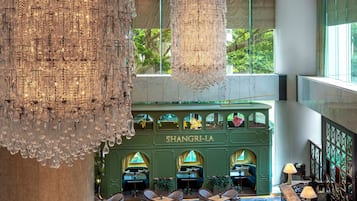 Un hall d’entrée spacieux, doté d’un plafond haut, de lustres somptueux et d’un espace détente avec des tables et des chaises.