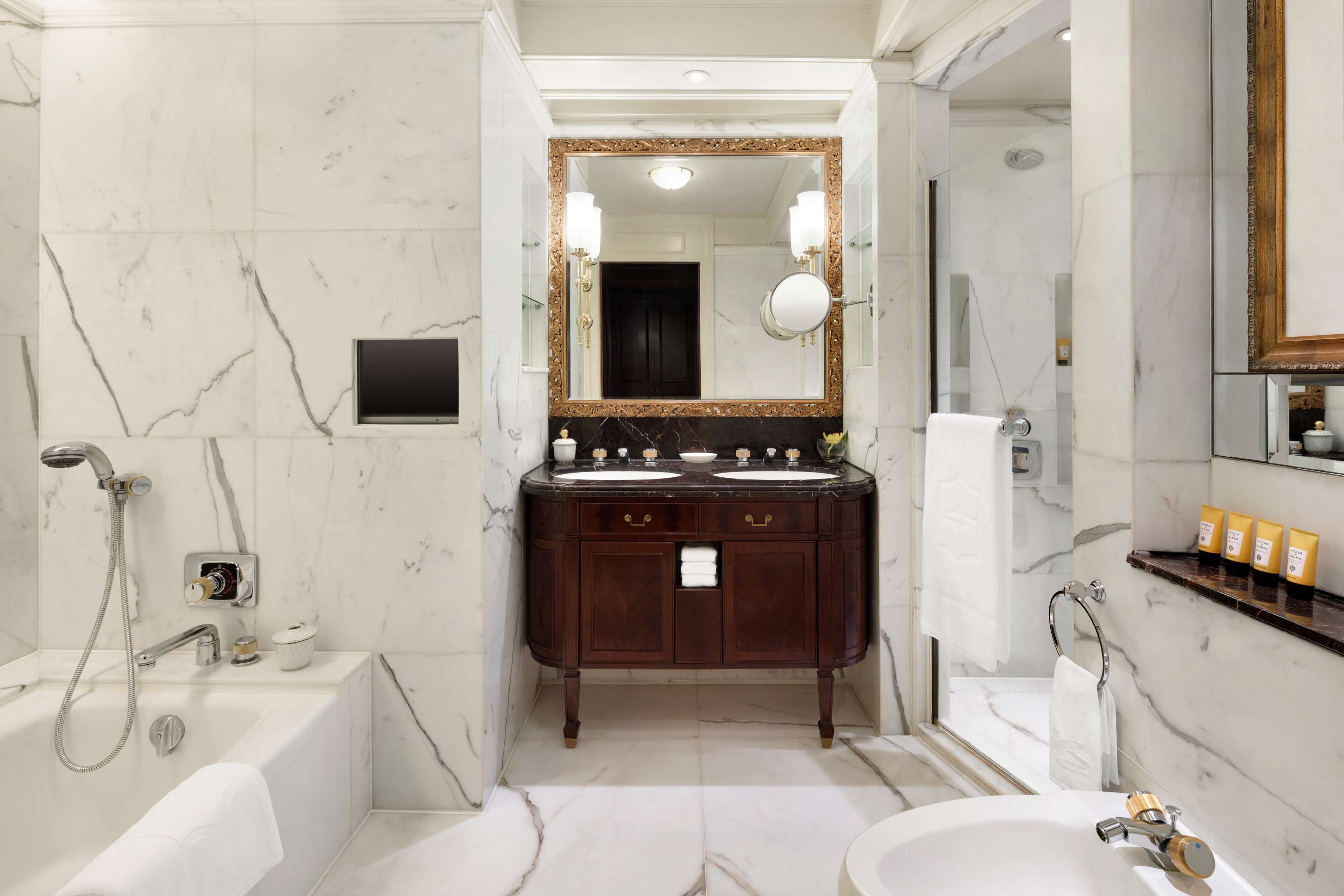 A bathroom with a marble floor, a double sink vanity, a large mirror, a bathtub, and a shower area.