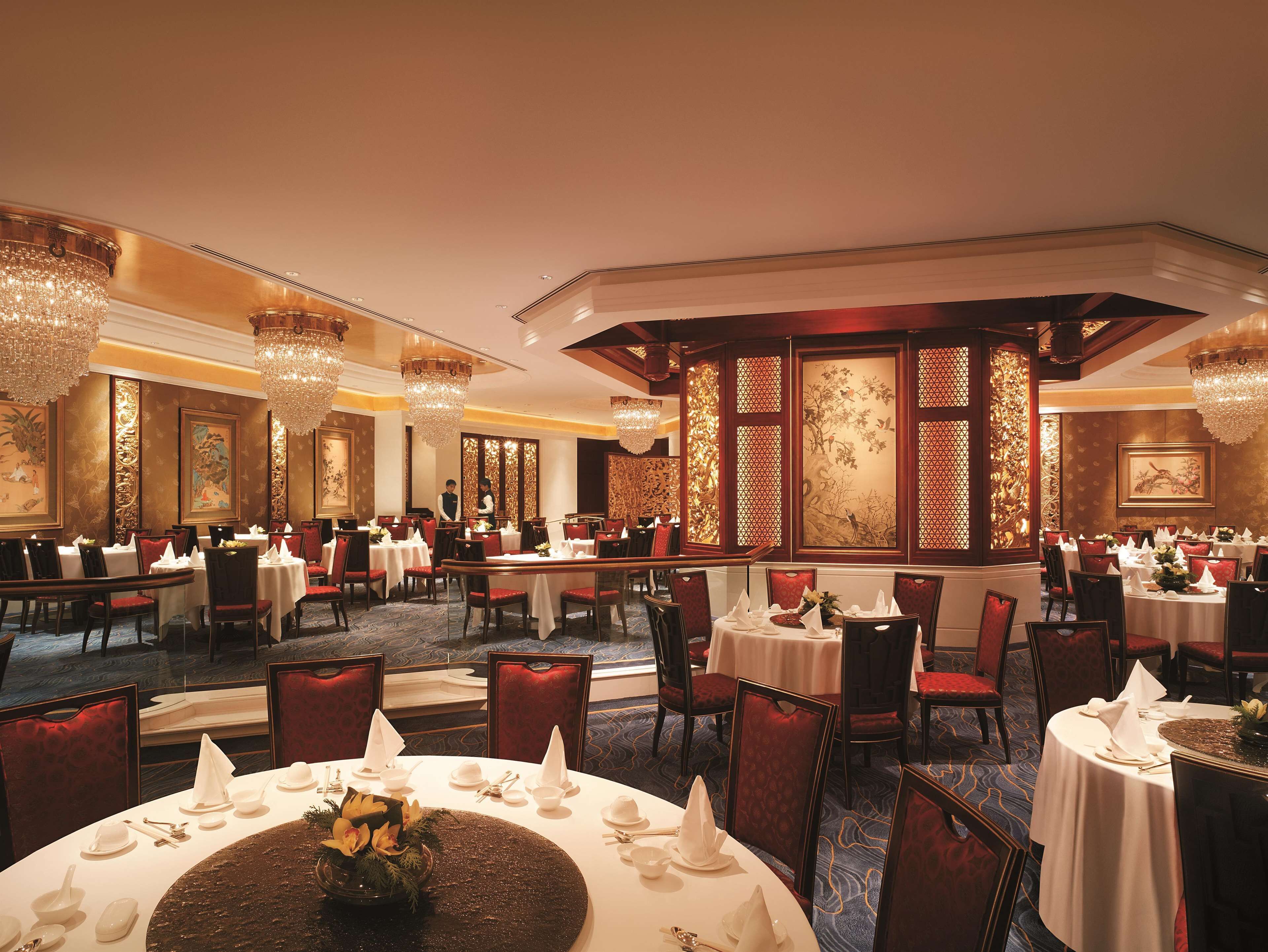 A formal dining room with multiple tables set for service, elegant chandeliers, and traditional decor.