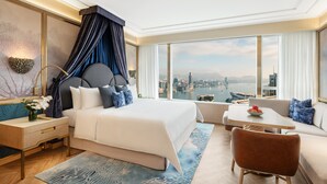 A modern hotel room with a large bed, a sitting area with a view of the city, and a nightstand with a lamp. - Island Shangri-La, Hong Kong (Hong Kong)