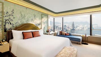 Habitación de hotel con una cama grande, zona de estar y vistas a un paisaje urbano a través de amplios ventanales.
