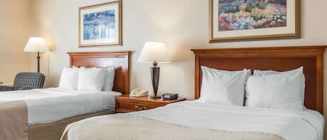 Una habitación de hotel con dos camas, una mesita de noche con lámpara, una silla y dos cuadros en la pared.