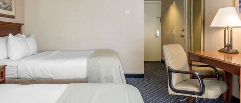 Habitación de hotel con dos camas, un escritorio con lámpara, una silla y una puerta que da a otra habitación.