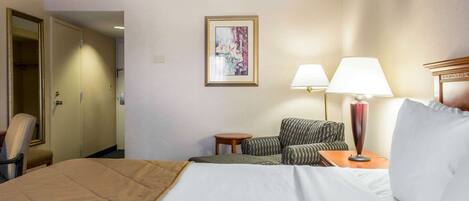Habitación de hotel con cama, dos sillas, una mesita, una lámpara y un cuadro en la pared.