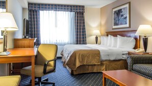 A hotel room with a bed, two bedside tables with lamps, a desk with a chair, a sofa, and a large window with curtains. - Clarion Hotel & Conference Center Ronkonkoma MacArthur Airport (Ronkonkoma)
