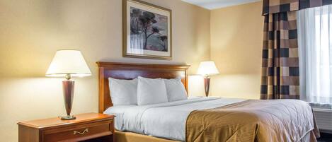 Habitación de hotel con una cama grande, dos mesitas de noche con lámparas, un cuadro enmarcado en la pared y una ventana con cortinas.