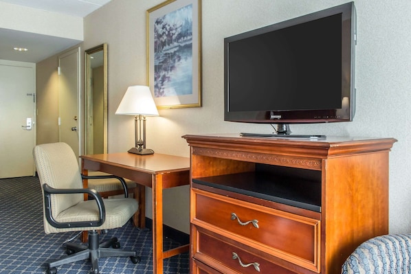 Une chambre d’hôtel avec un bureau en bois, une chaise, un téléviseur, une lampe et un tableau encadré au mur.
