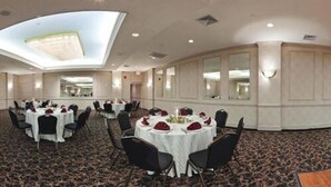 A conference room with round tables, black chairs, and a patterned carpet. - Clarion Hotel & Conference Center Ronkonkoma MacArthur Airport (Ronkonkoma)