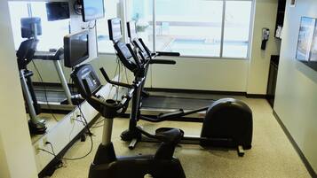 Un gimnasio con equipo cardiovascular, cinta de correr y bicicleta estática.