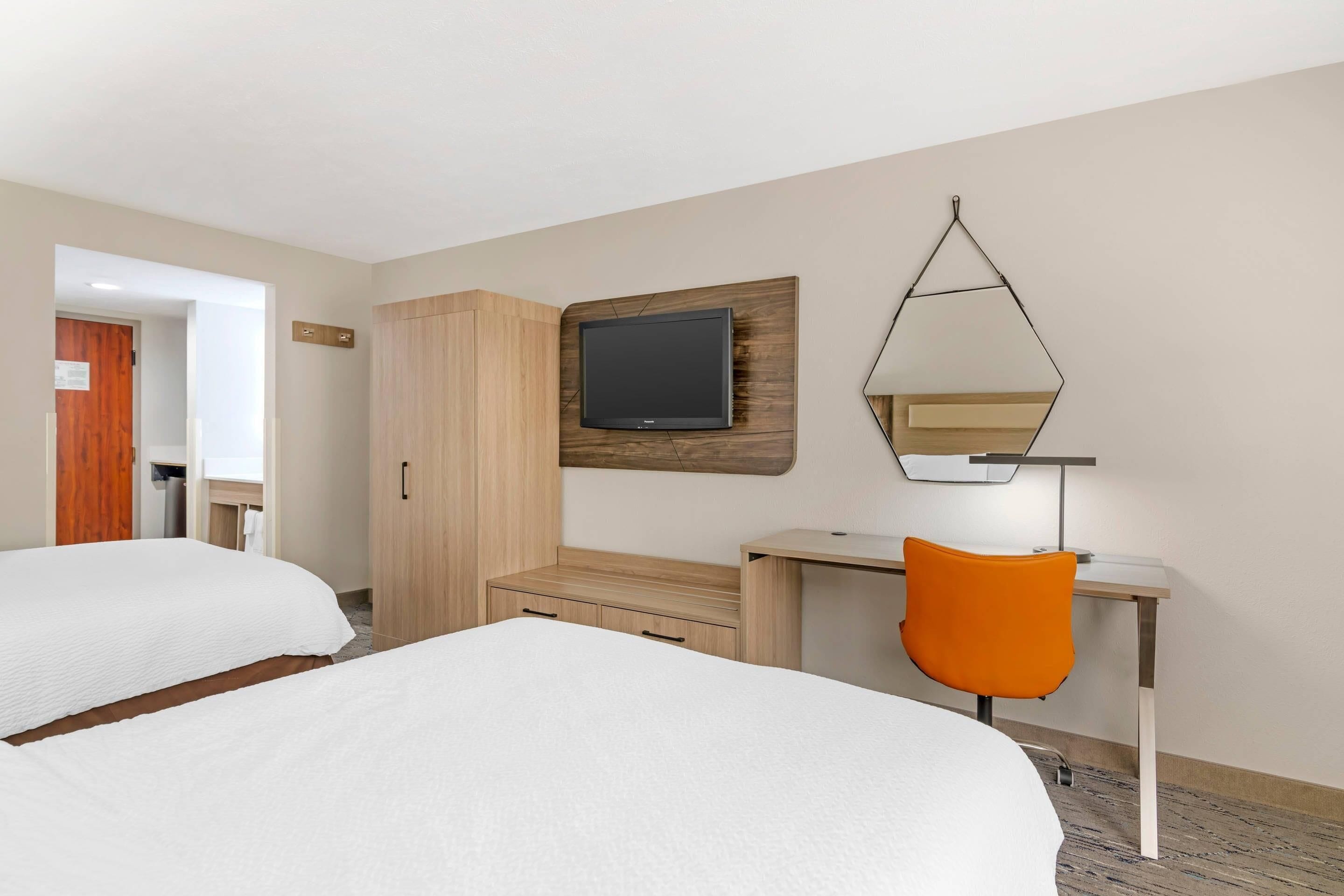 A hotel room with two beds, a desk, a chair, a TV, and a mirror.