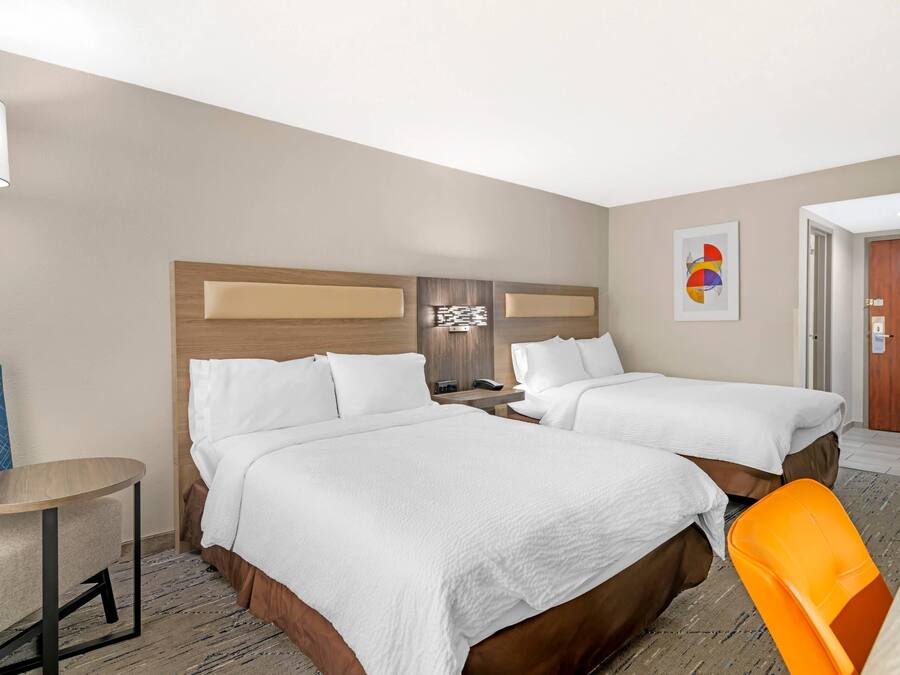Habitació d'hotel amb dos llits, una taula petita, una cadira i una làmpada.