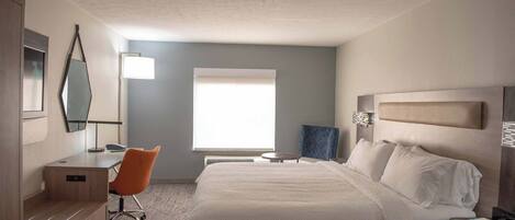 A hotel room with a bed, a desk, an orange chair, a window, and a lamp.
