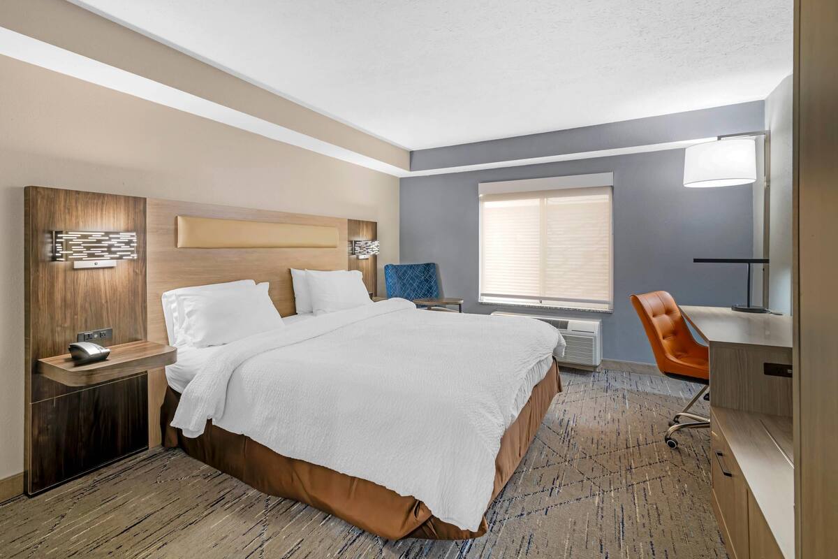 Een hotelkamer met een groot bed, een bureau met stoel, een raam met zonwering en een aan de muur bevestigde televisie.