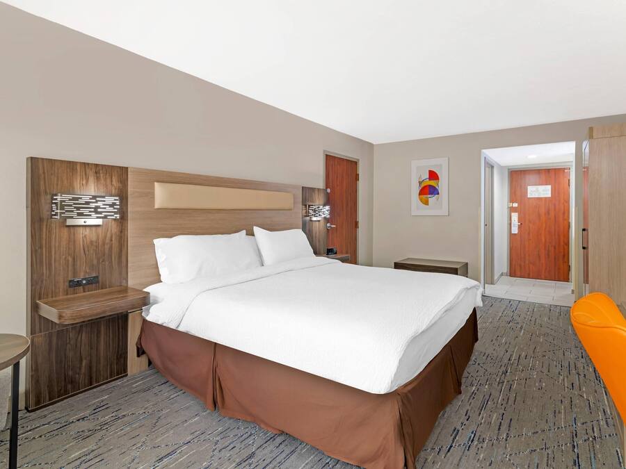 Une chambre d’hôtel avec un grand lit, une tête de lit en bois, un téléviseur à écran plat, un bureau et une chaise.