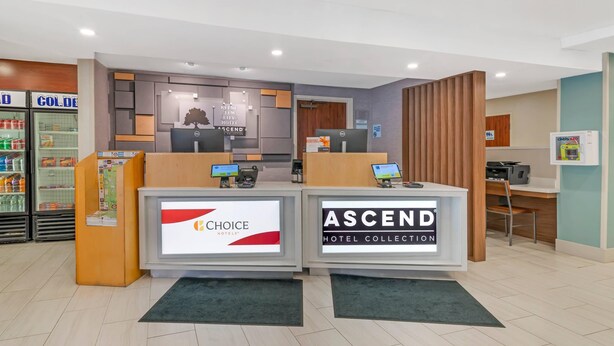 A hotel reception area with two counters labeled 'Choice Hotels' and 'Ascend Hotel Collection'. There are vending machines and a refrigerator with beverages. - Keene Elm City Hotel, an Ascend Collection Hotel (Keene)